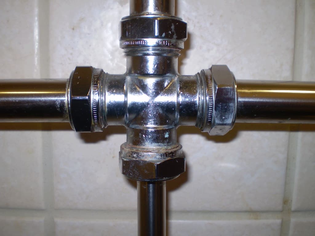 Chrome cross pipe fitting on a tiled bathroom wall