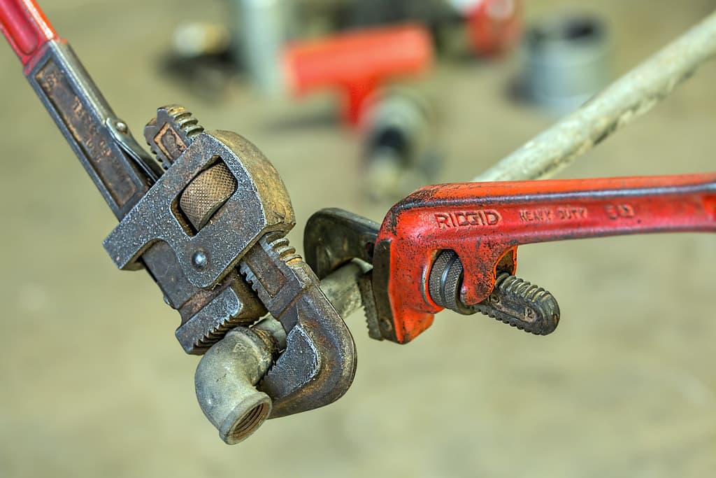 Two pipe wrenches fitted to a copper pipe elbow joint